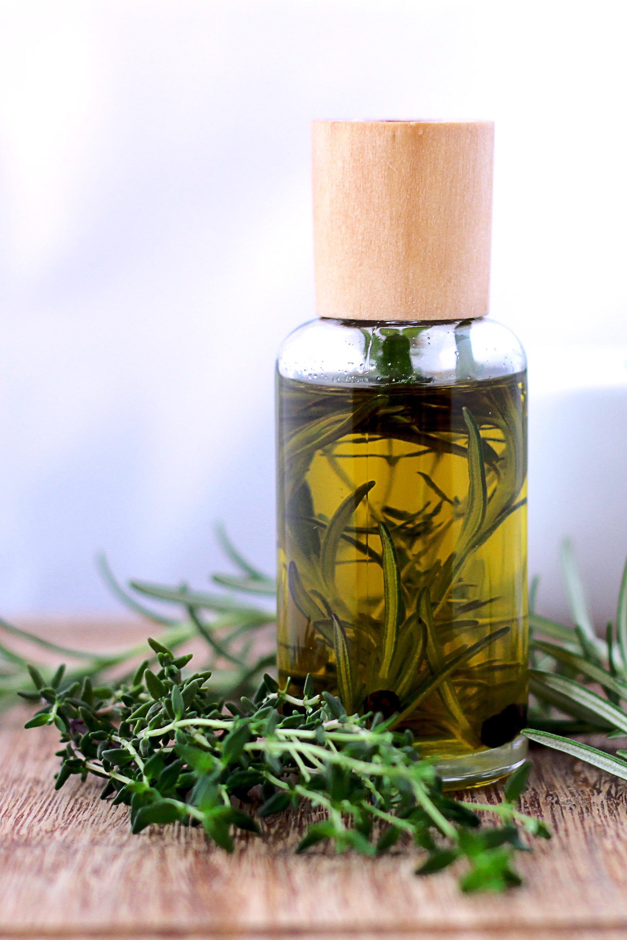 Glass bottle of rosemary and thyme infused oil on wooden table – natural botanical extract used in Deoxylocks 2ddr hydrogel for healthy scalp and hair growth