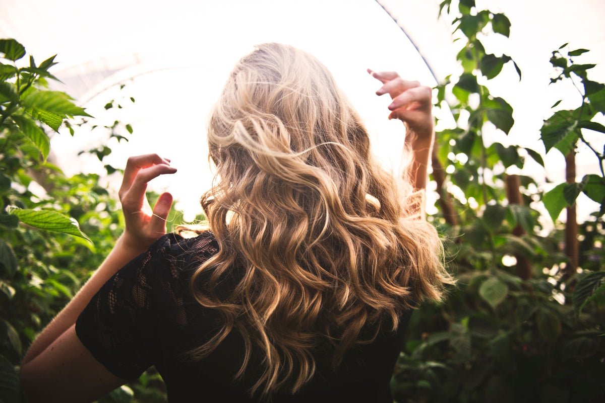 Blonde woman with curly hair surrounded by lush greenery, enjoying a sunny day