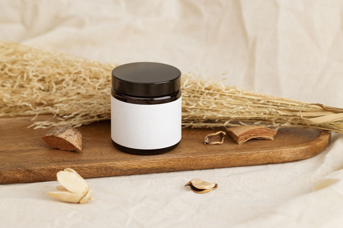 Natural cosmetic jar with blank label on a rustic wooden tray surrounded by dried herbs