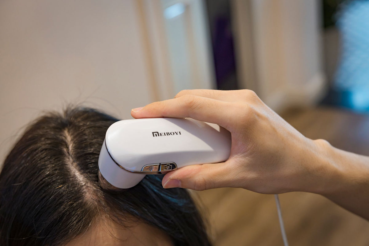 Close-up of a handheld device examining a person's scalp indoors