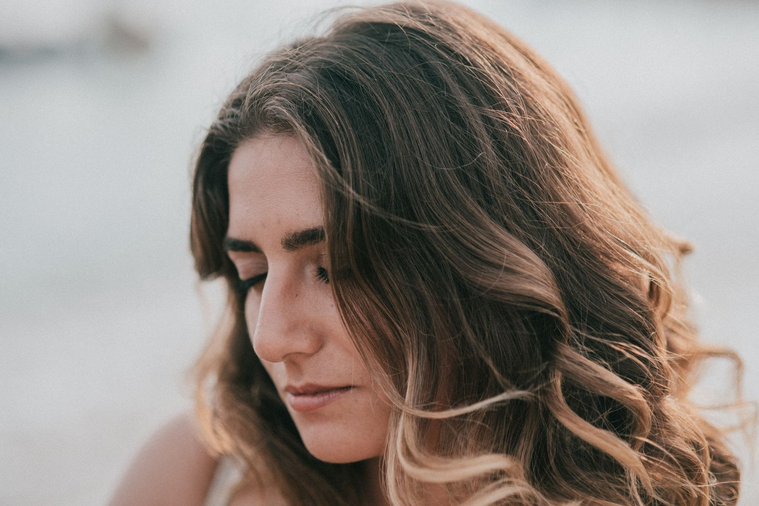 Close-up portrait of a young woman with wavy blonde hair and eyes closed, conveying serenity