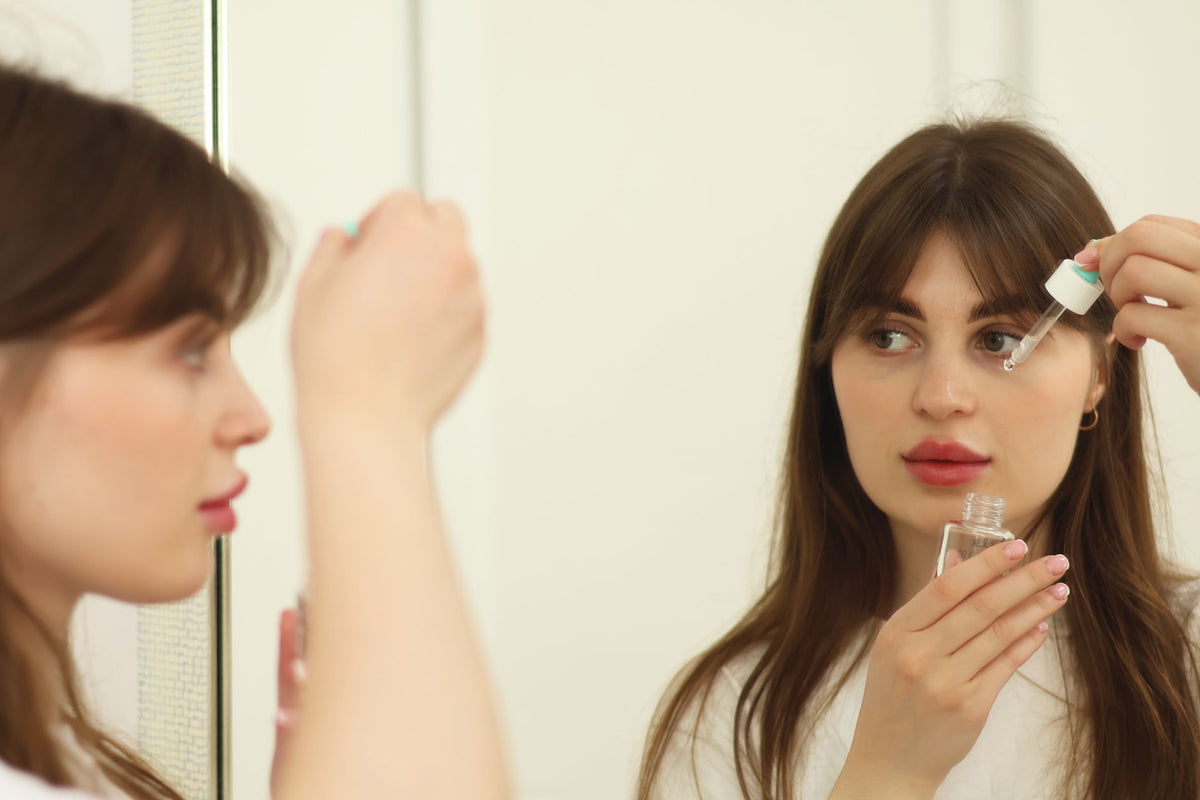 A young woman applying skincare serum in front of a mirror indoors. Perfect for beauty and self-care themes