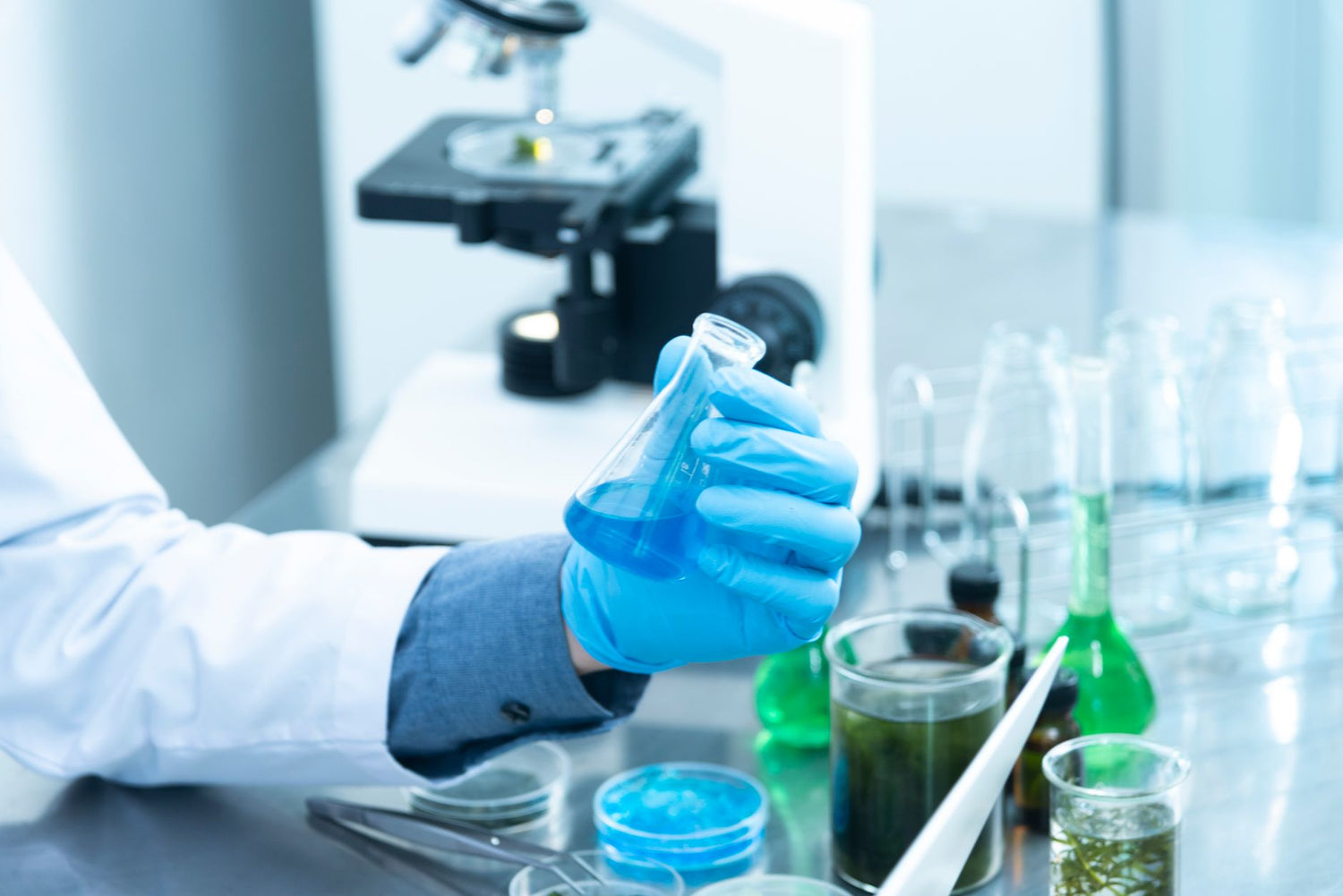 Scientist in gloves analyzing blue liquid in a laboratory setting with microscope and glassware