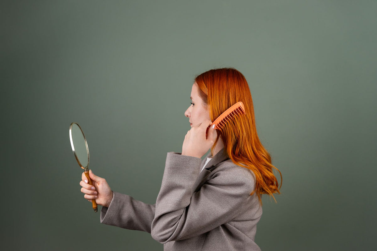 Side profile of a woman combing her hair and looking in a handheld mirror