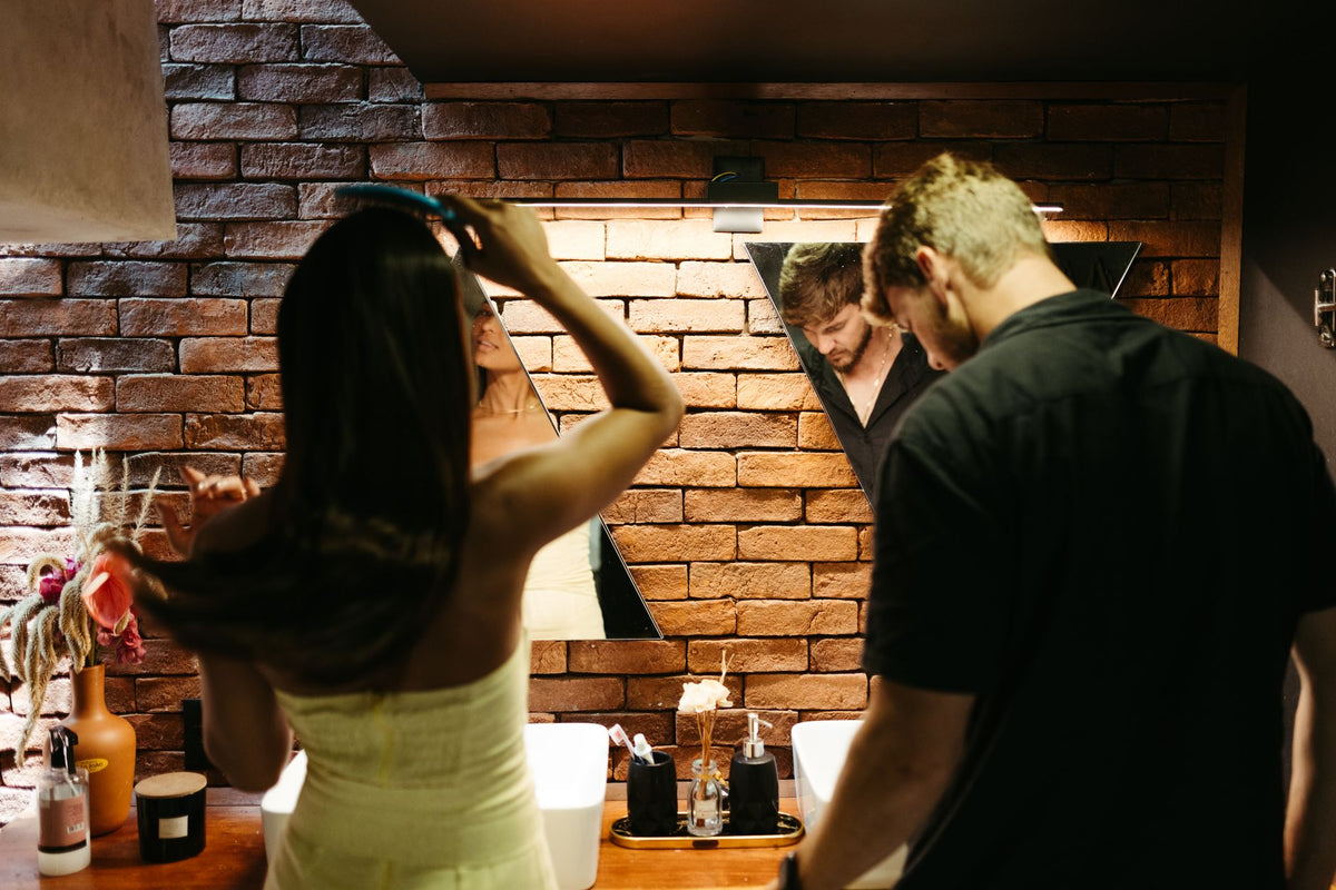A young couple preparing in a stylish bathroom with exposed brick walls and unique mirrors