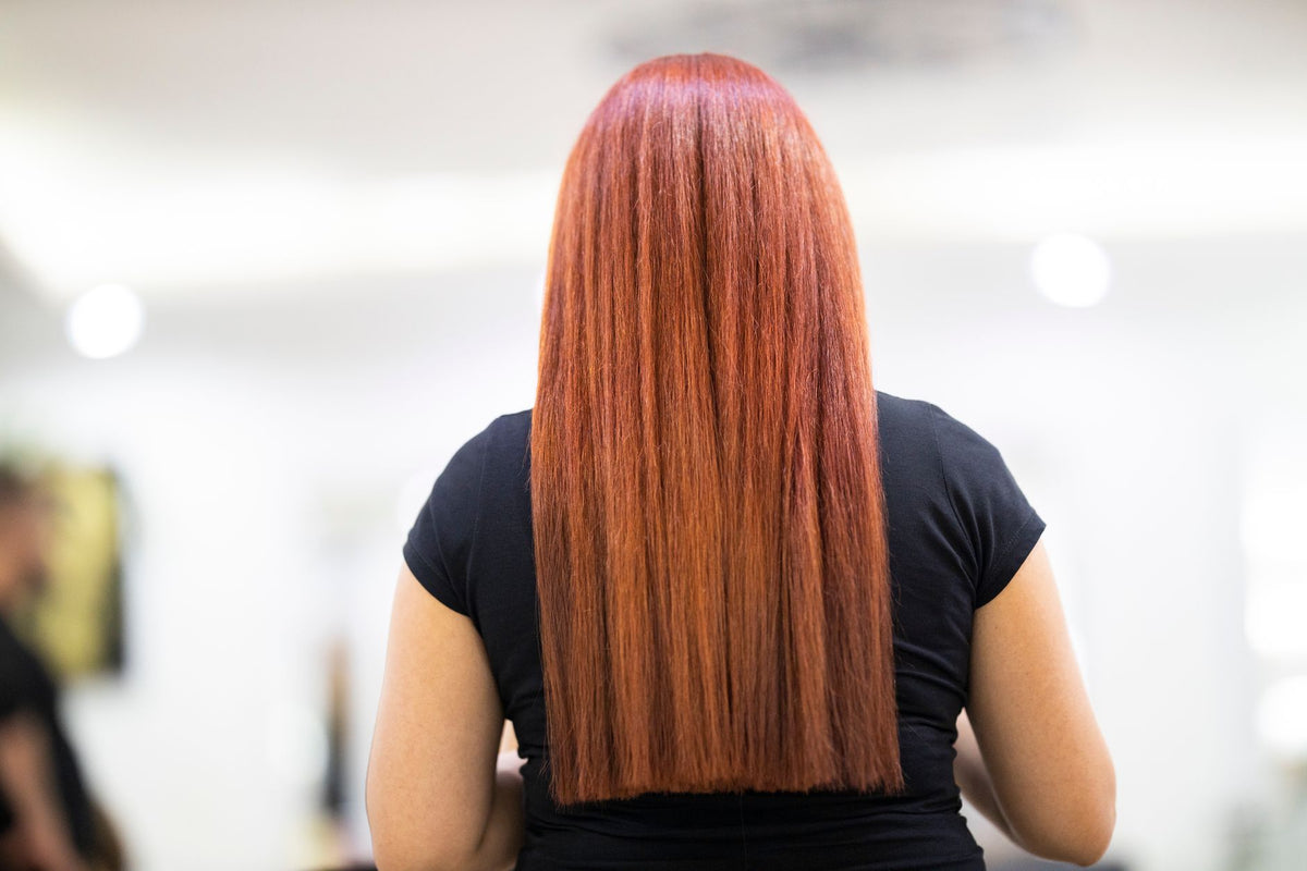 A woman with straight, vibrant red hair seen from the back, showcasing a fresh hairstyle in a professional salon