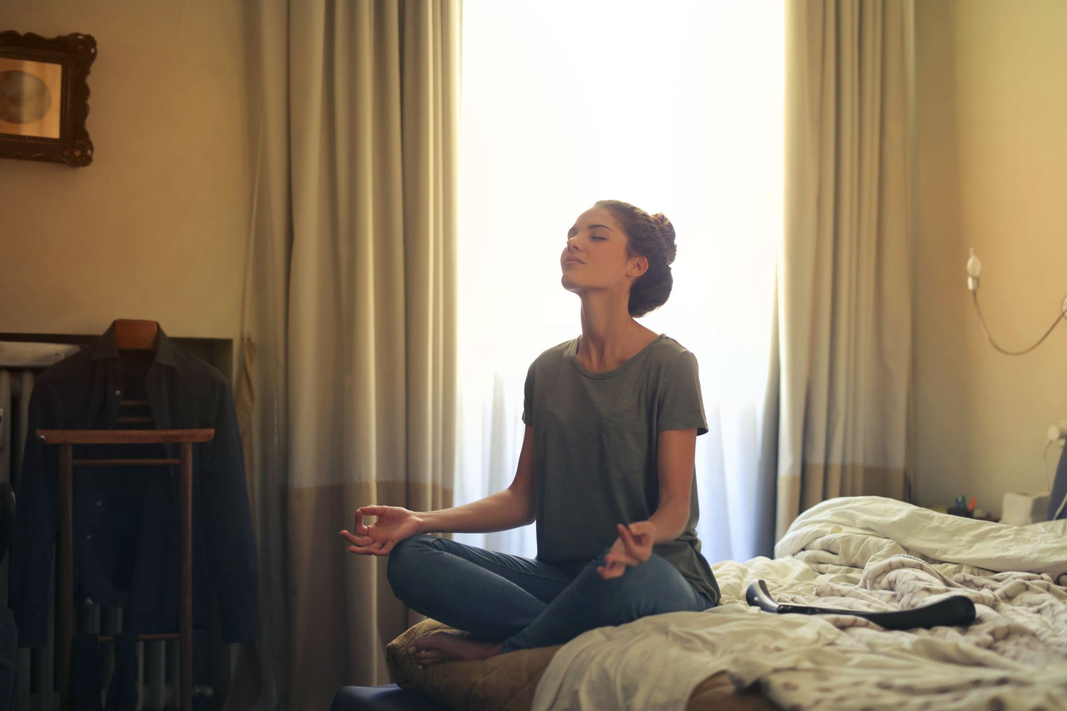 Adult woman practicing meditation on her bed surrounded by a calm bedroom atmosphere