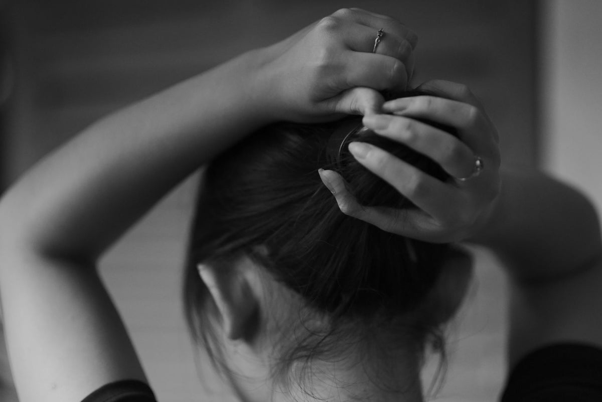 A woman ties her hair in a bun, depicted in a black and white photograph, evoking a classic and serene mood