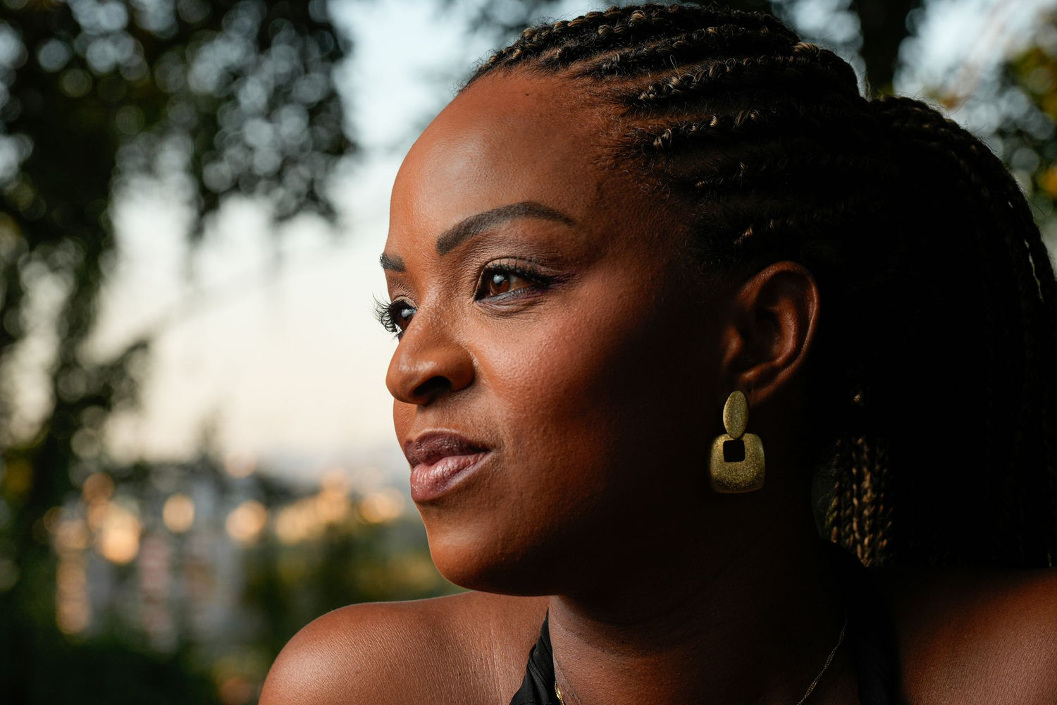 Close-up portrait of a woman with braided hair and earrings in a natural outdoor setting