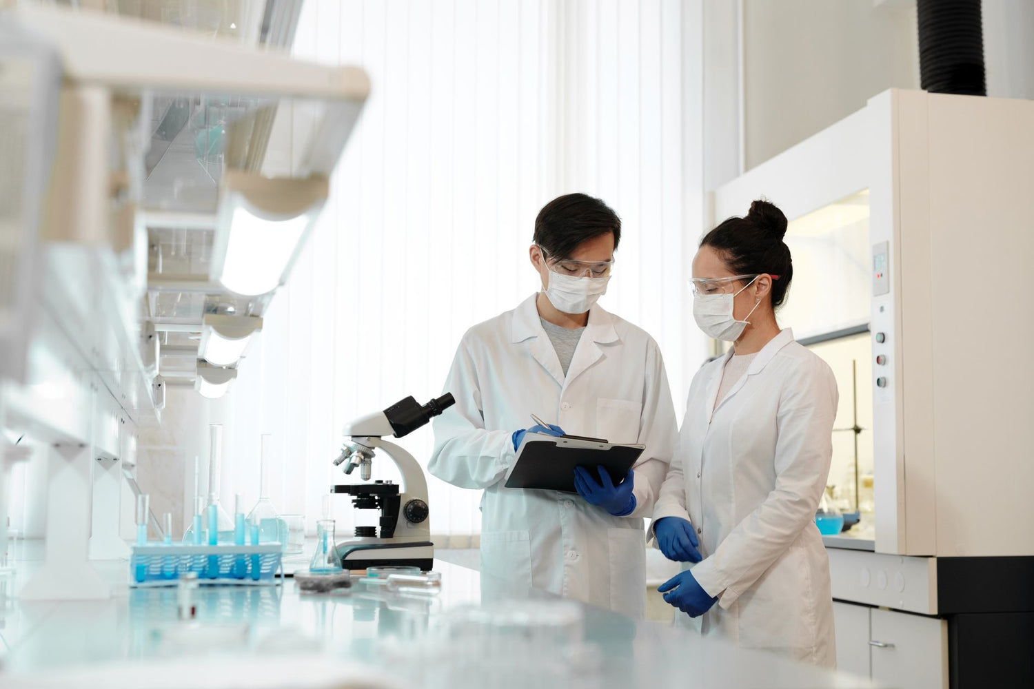 Two scientists in a laboratory wearing masks, discussing research with a microscope