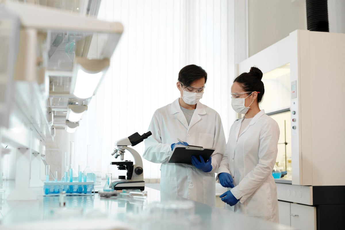 Two scientists in a laboratory wearing masks, discussing research with a microscope