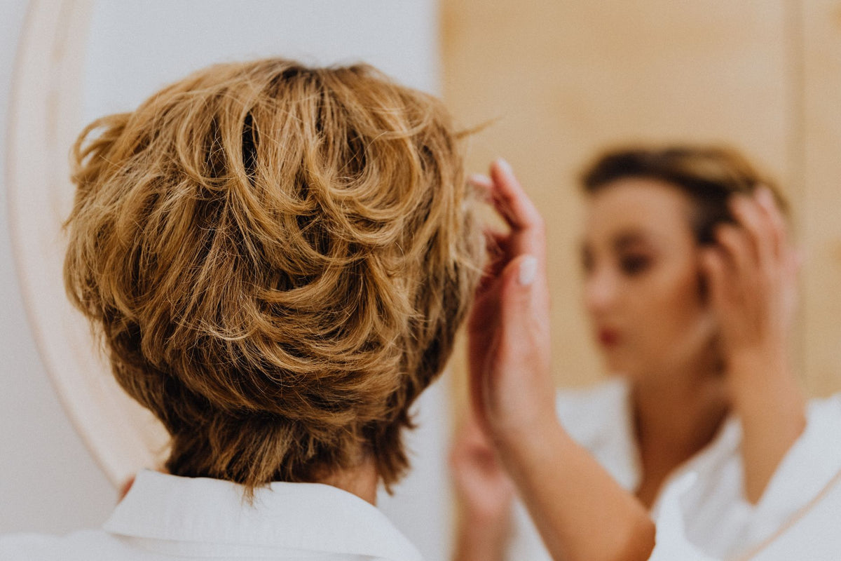 Back view of a woman styling her short hair while looking in the mirror