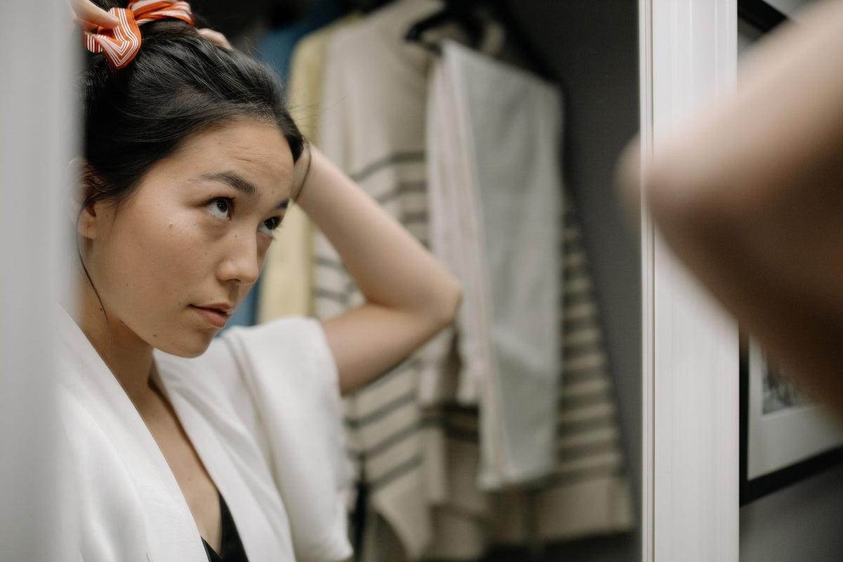Woman in bathrobe adjusts hair in front of a bathroom mirror