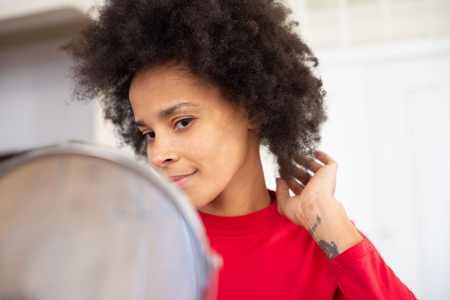 Confident woman with afro hairstyle glancing in the mirror, adjusting her hair indoors