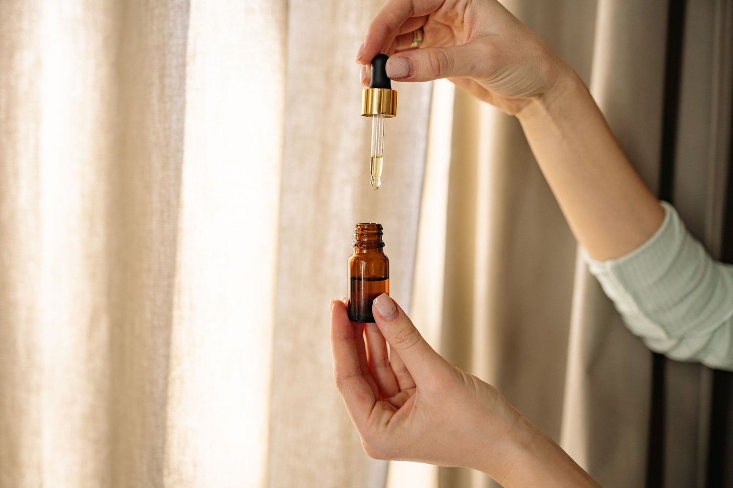 Close-up of hands holding a dropper and amber bottle for skincare product