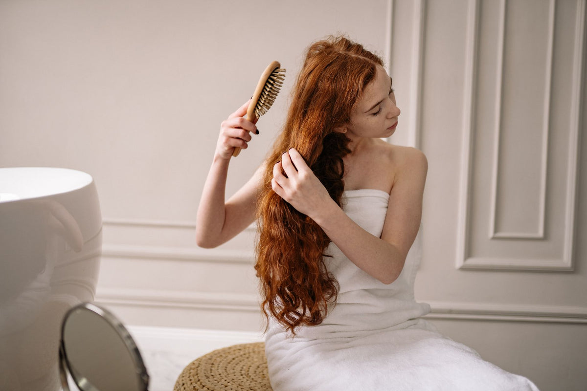 Woman with long red hair wrapped in a towel combing her hair in an elegant bathroom setting