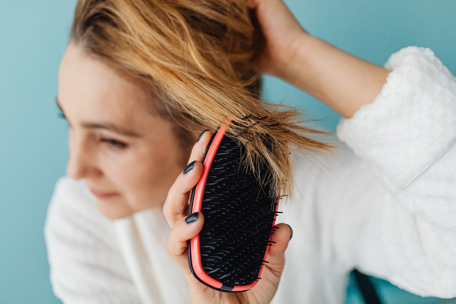Close-up of a woman brushing her blonde hair with a red hairbrush indoors