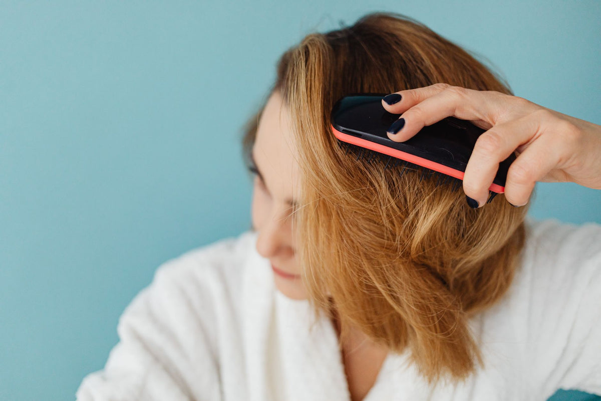 Close-up of a woman with brown hair brushing her hair in a bathrobe, representing a daily grooming routine