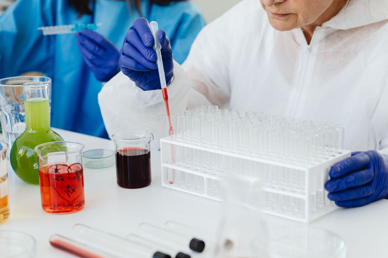 Female scientist in lab coat using pipette on test tubes, focusing on colorful chemical analysis