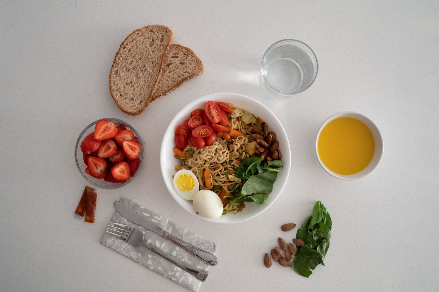 A balanced meal featuring a variety of healthy ingredients including noodles, eggs, almonds, strawberries, and fresh ...