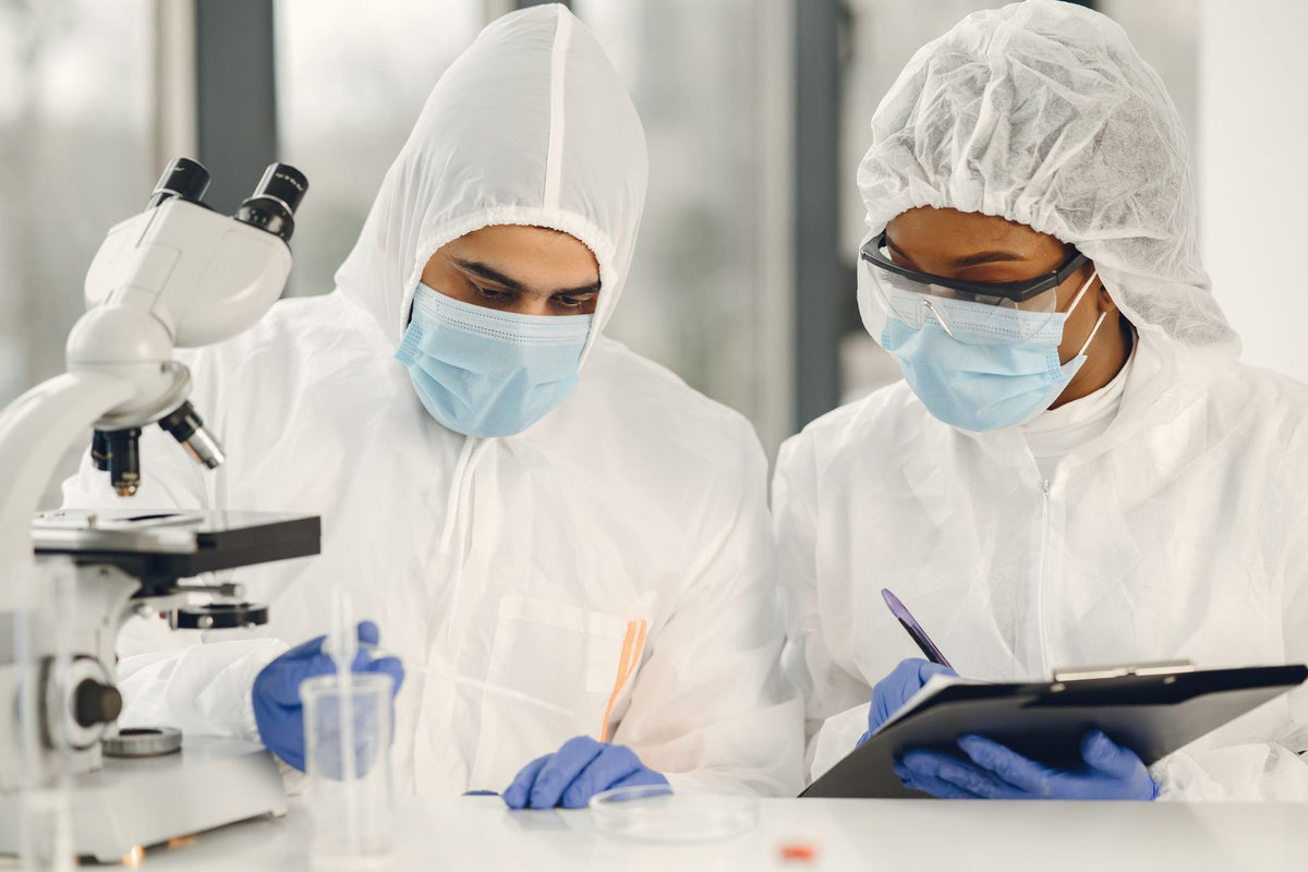 Two scientists in hazmat suits working with a microscope and notes in a laboratory setting