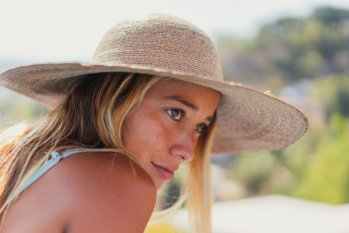 Close-up portrait of a thoughtful woman wearing a sun hat outdoors