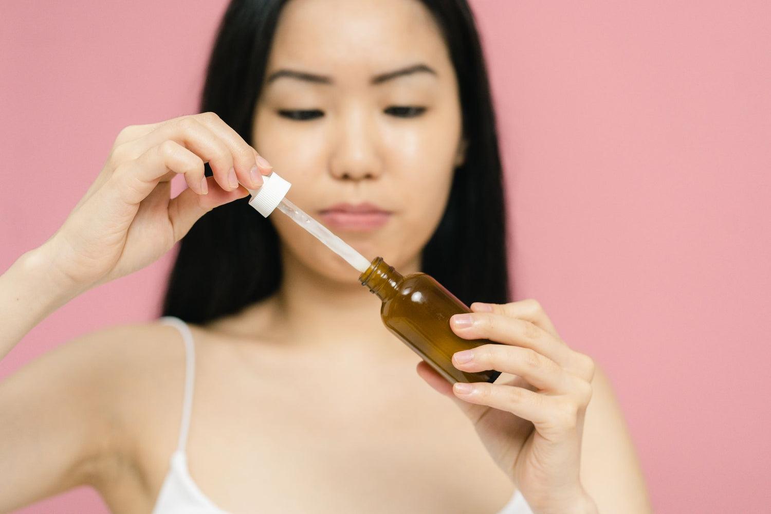 Close-up of a woman holding a serum bottle with a dropper, focusing on skincare