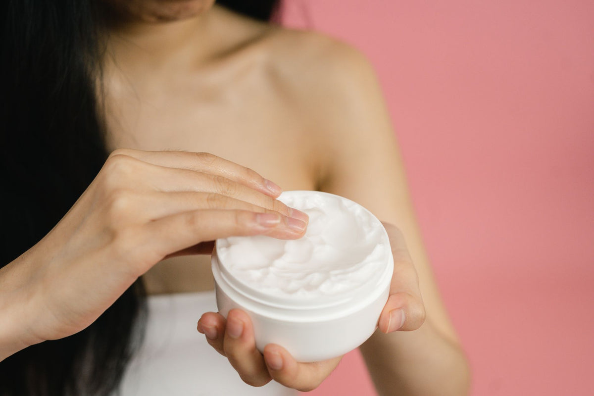 Close-up of a woman applying white cream from a jar against a pink background